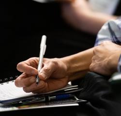 A hand holding a pen over a pad of paper
