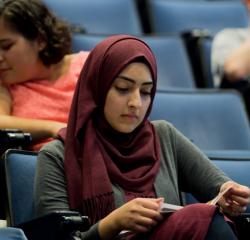 A student wearing a hijab reading a book in a lecture hall