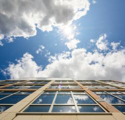 Looking up the side of a campus building into a blue sky with sun and clouds