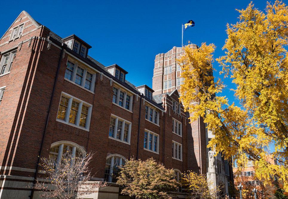 The Michigan Union and a nearby tree covered in golden leaves stand against a clear blue sky.