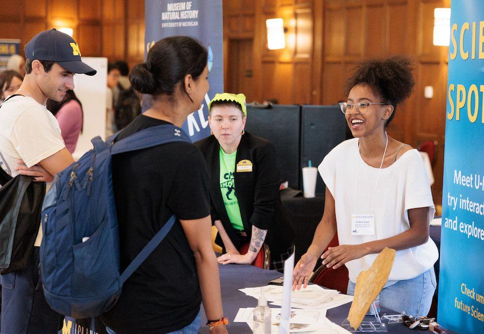 A presenter from the University of Michigan Museum of Natural History speaks to a pair of graduate students at the Rackham Graduate Student Resource Fair.