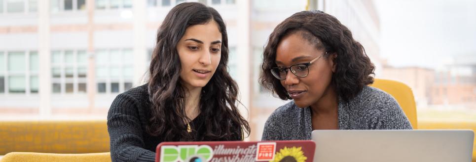 Two people talking while looking at laptops