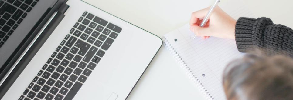 Overhead view of someone writing on a pad of paper in front of an open laptop