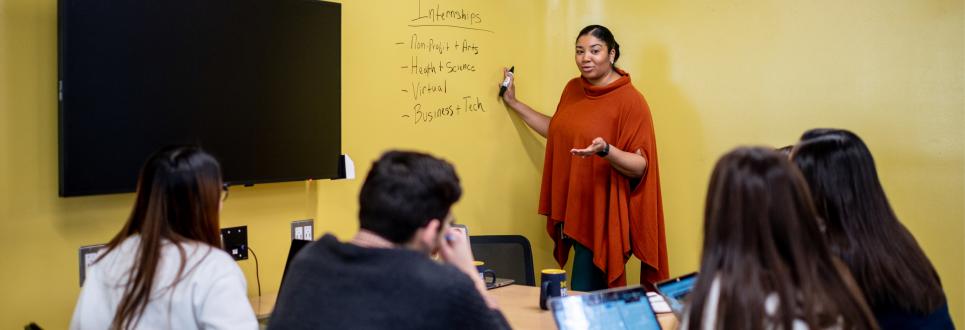 A faculty member writing on a board while teaching in a classroom