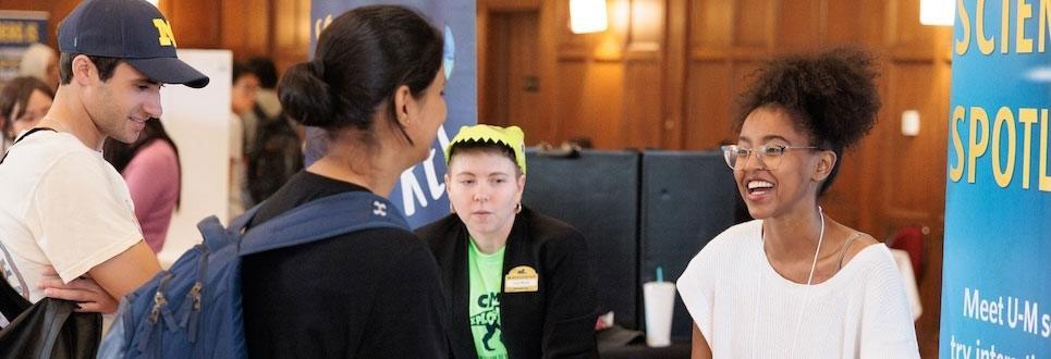 A presenter from the University of Michigan Museum of Natural History speaks to a pair of graduate students at the Rackham Graduate Student Resource Fair.